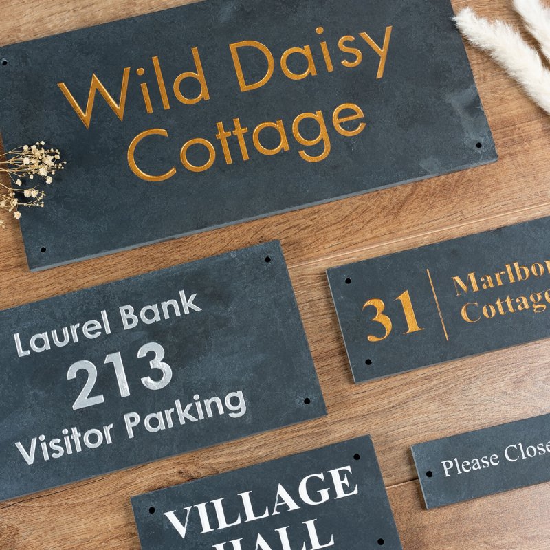 Collection of personalised slate house signs featuring engraved text in various designs and fonts. Ideal for enhancing property entrances with durable, weather-resistant designs.